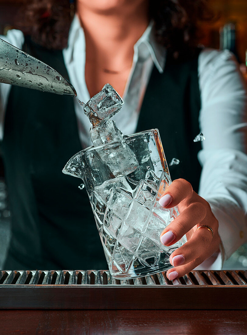 Barkeeper gibt Eiswürfel in ein Cocktailglas