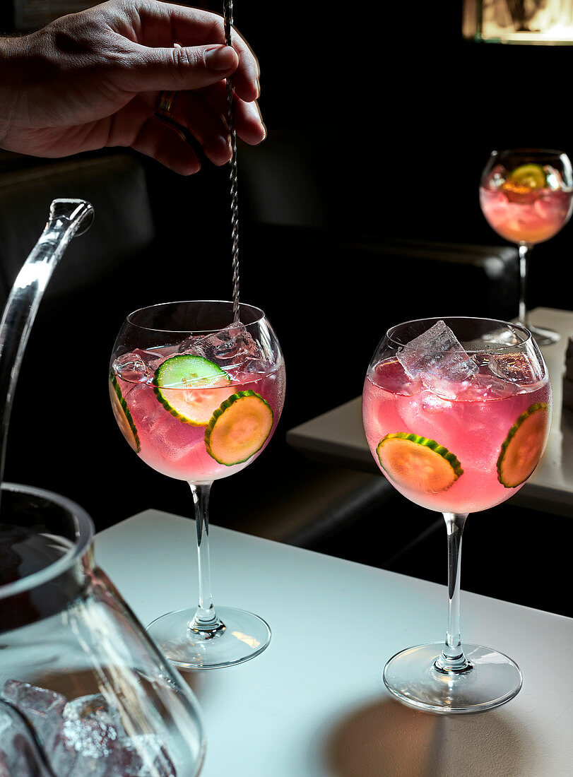 Pinkfarbener Cocktail mit Gurkenscheiben und Eiswürfeln