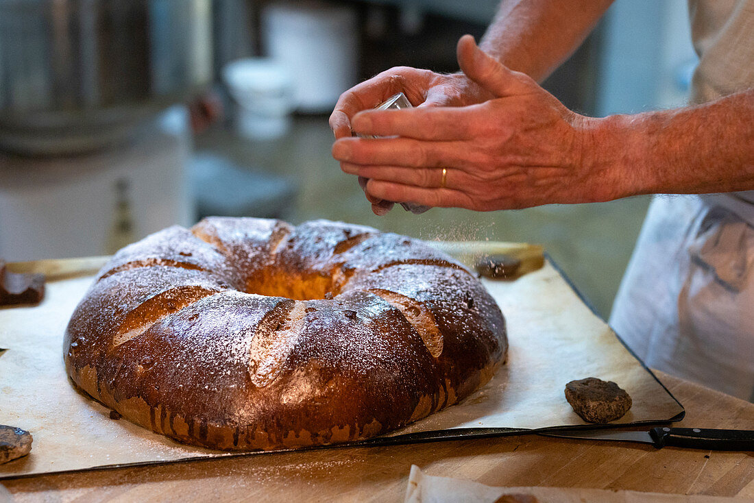 Bäcker bestreut traditionell hergestellte Brioche mit Puderzucker