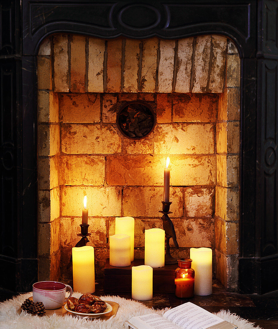 Tee und Gebäck vor Kamin mit brennenden Kerzen