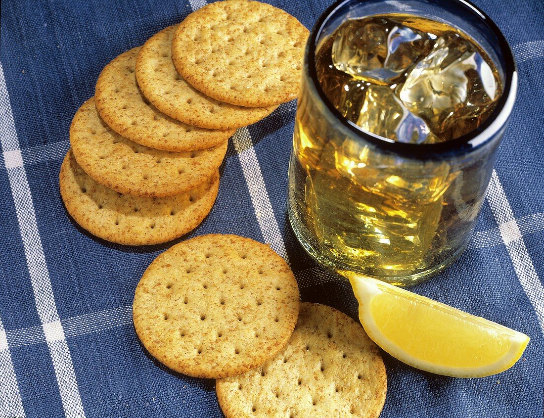 Ein Glas Whiskey mit Eiswürfeln; Cracker & Zitronenschnitz