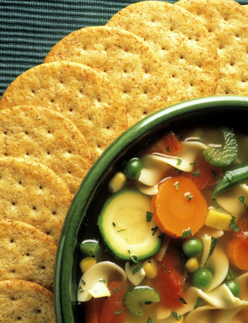 A Bowl of Vegetable Noodle Soup with Crackers