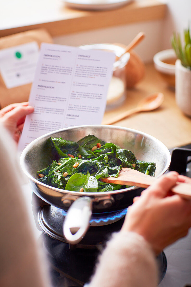 Woman preparing fresh spinach with pine nuts with recipe sheet