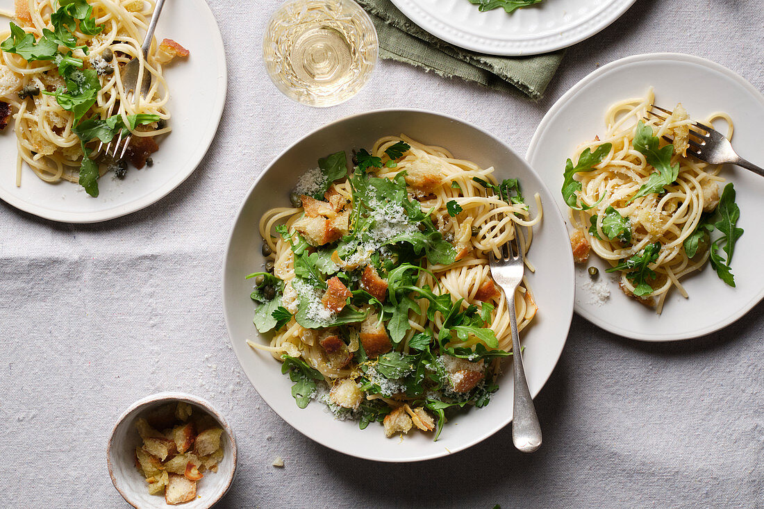 Spaghetti with bread pieces, fried garlic, arugula, and capers, served with grated cheese and lemon zest