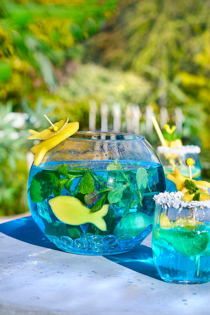 Cocktail Blue Lagoon serviert in Bowlegefäß und Gläsern auf Tisch im Freien