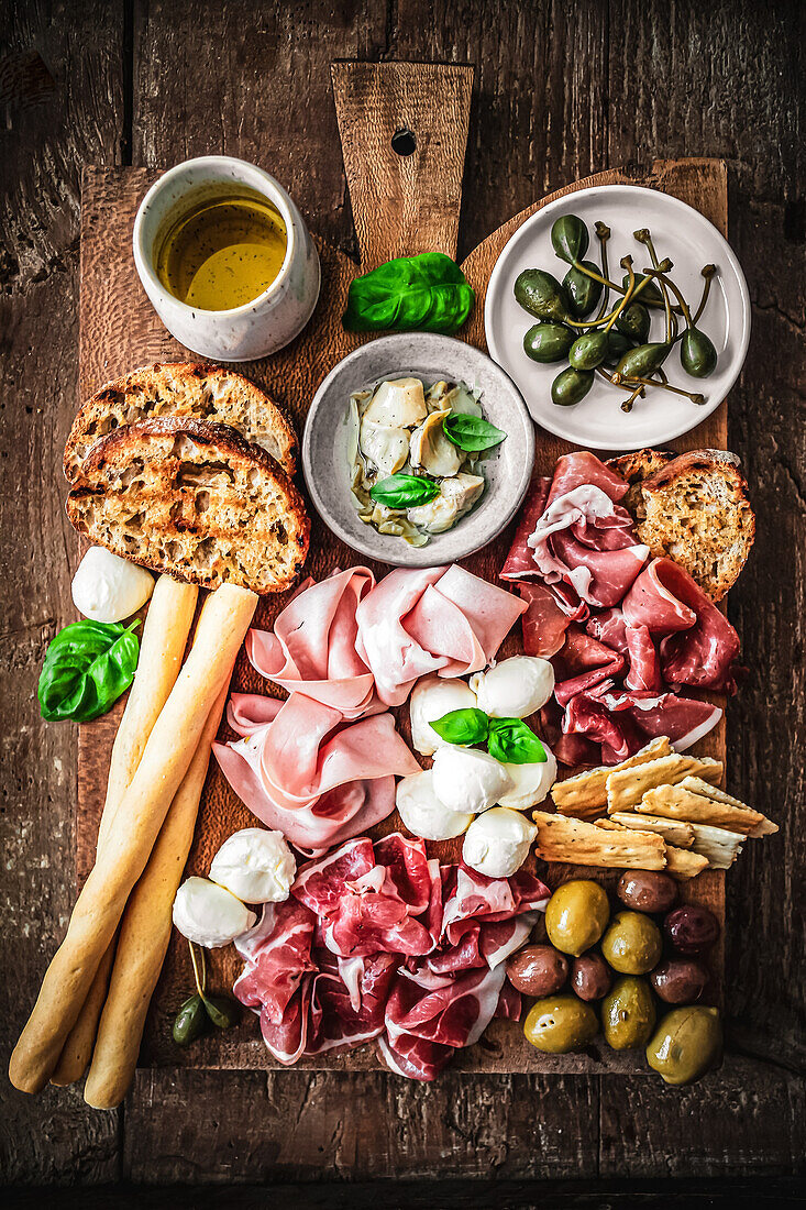 Antipasti-Platte mit Schinken, Kapern, Oliven, Artischocken, Mozzarella, Brot und Grissini