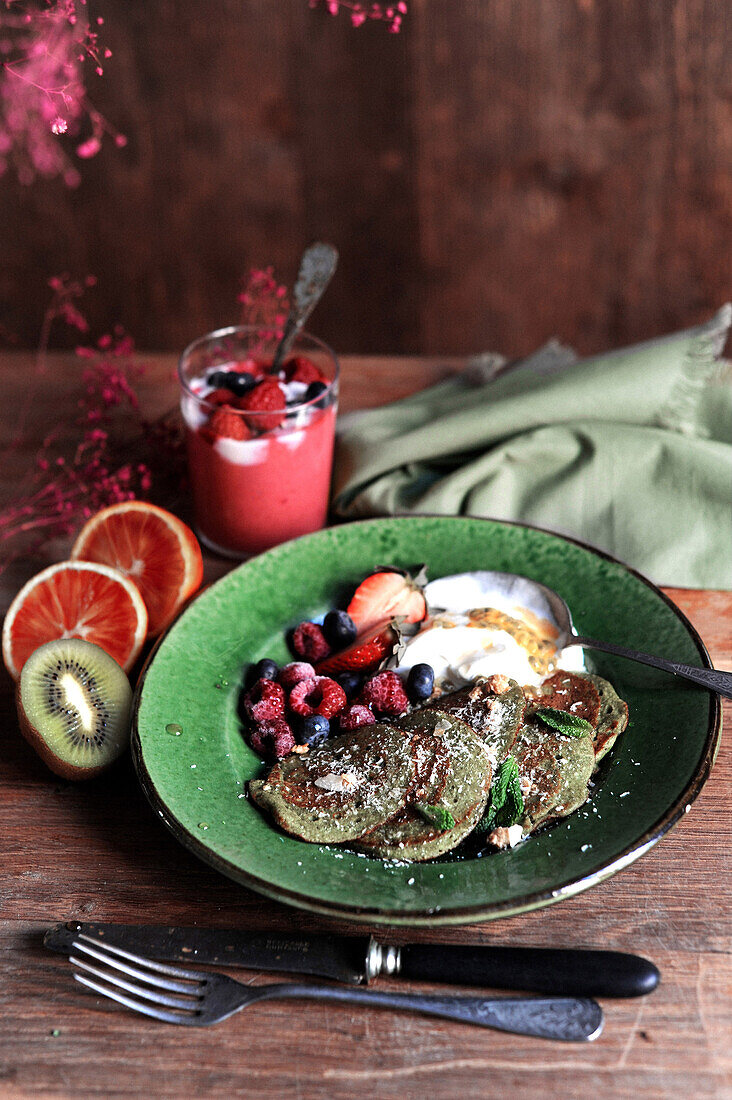 Green spinach pancakes with red berries and sour cream