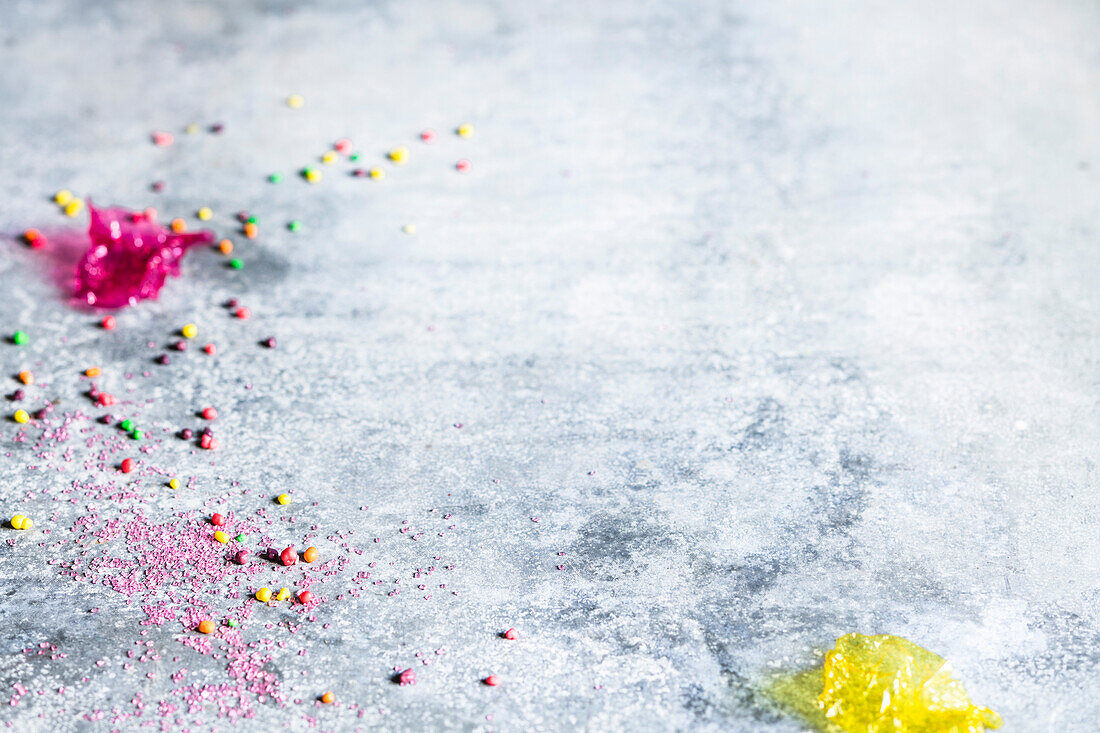 Colorful sugar sprinkles and candy wrappers on a grey background
