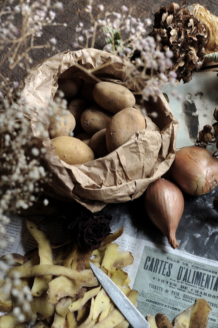 Potatoes in paper bag next to onions and potato skins on newspaper