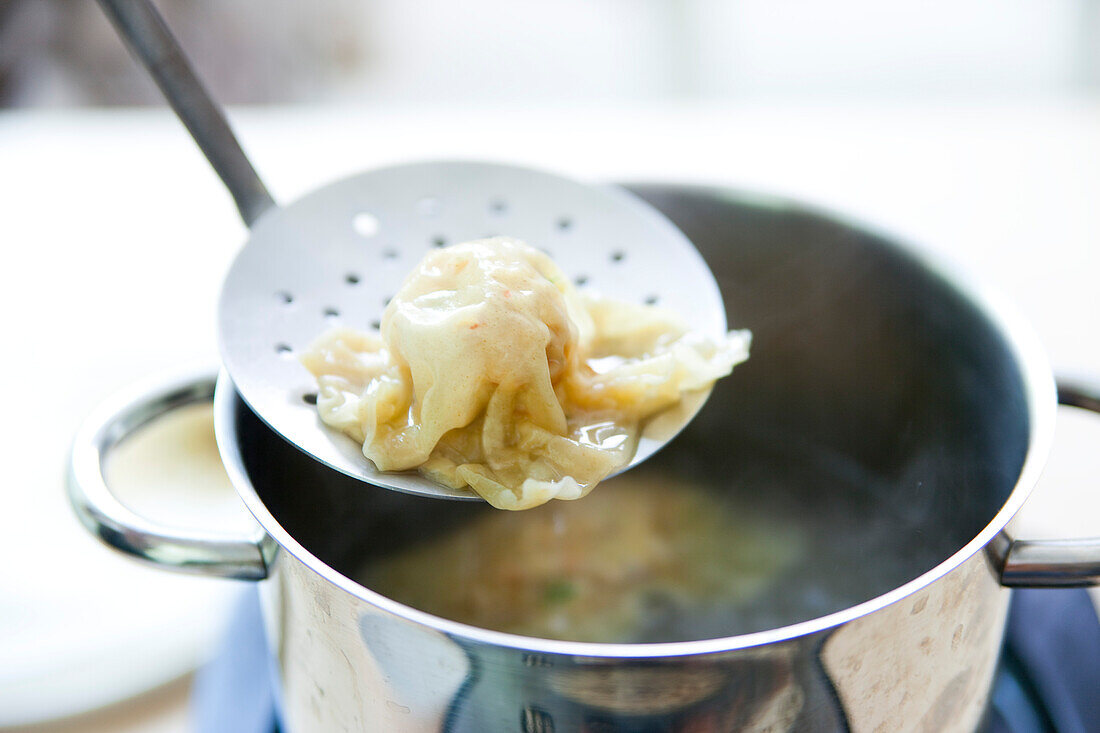 Krabbenravioli zubereiten: gekochte Ravioli auf Sieblöffel