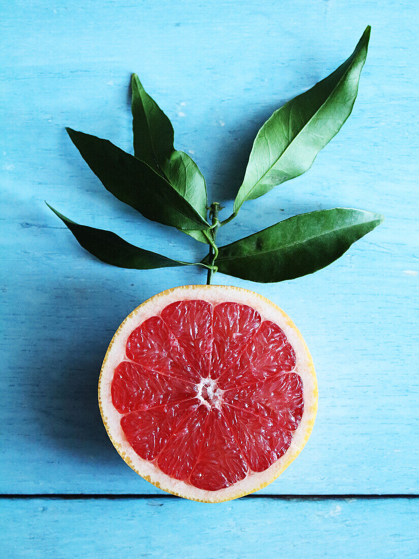 Pink grapefruit half with leaves against blue background