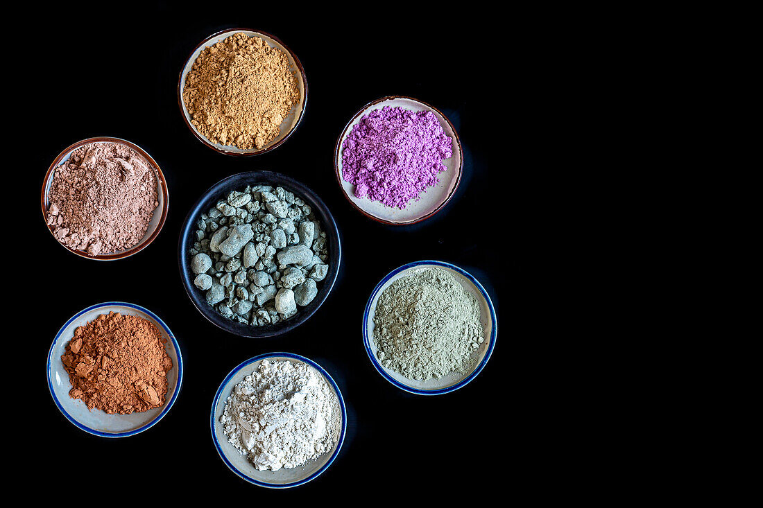 Various types of healing earth in small bowls on a black background