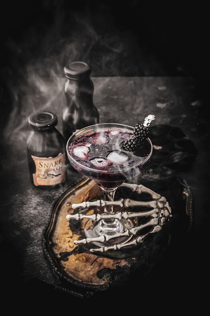 Halloween cocktail with blackberries, decorated with a skeleton hand