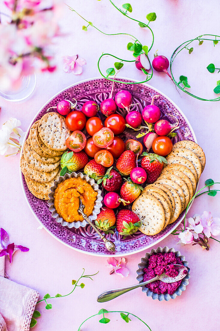Cracker, Sommergemüse, Sommerobst und Rote-Bete-Karotten-Dip auf Teller zum Aperitif