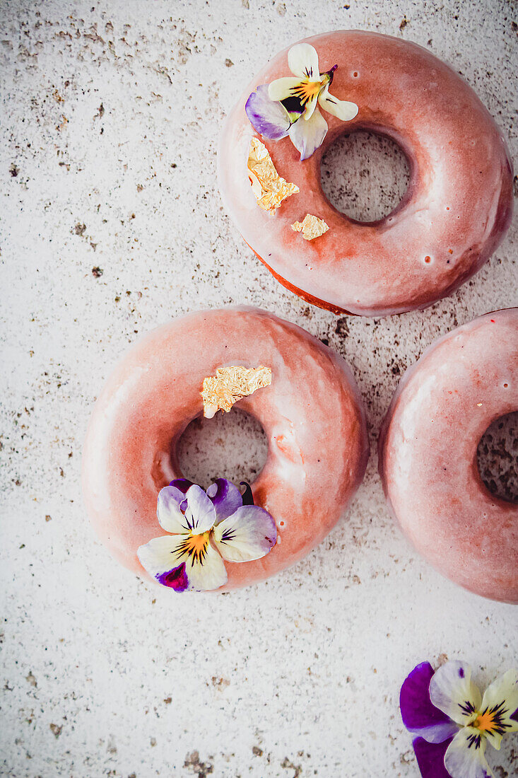 Donuts mit Zuckerglasur, Blattgold und Blüten dekoriert