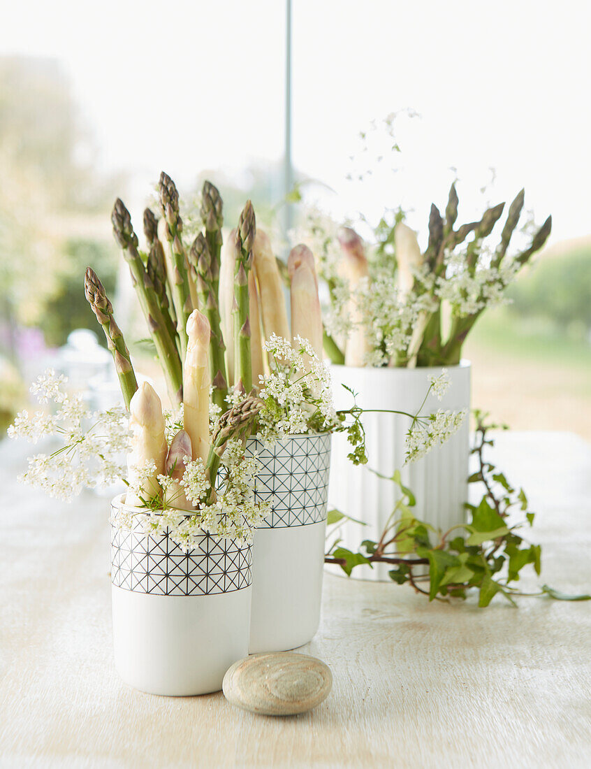 Frischer weißer und grüner Spargel mit Blütenzweigen in Vasen