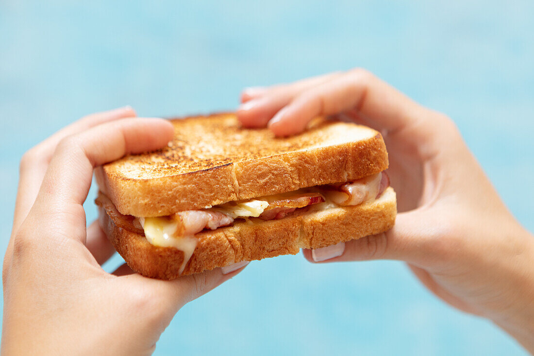 Hands holding a bacon and cheese croque monsieur