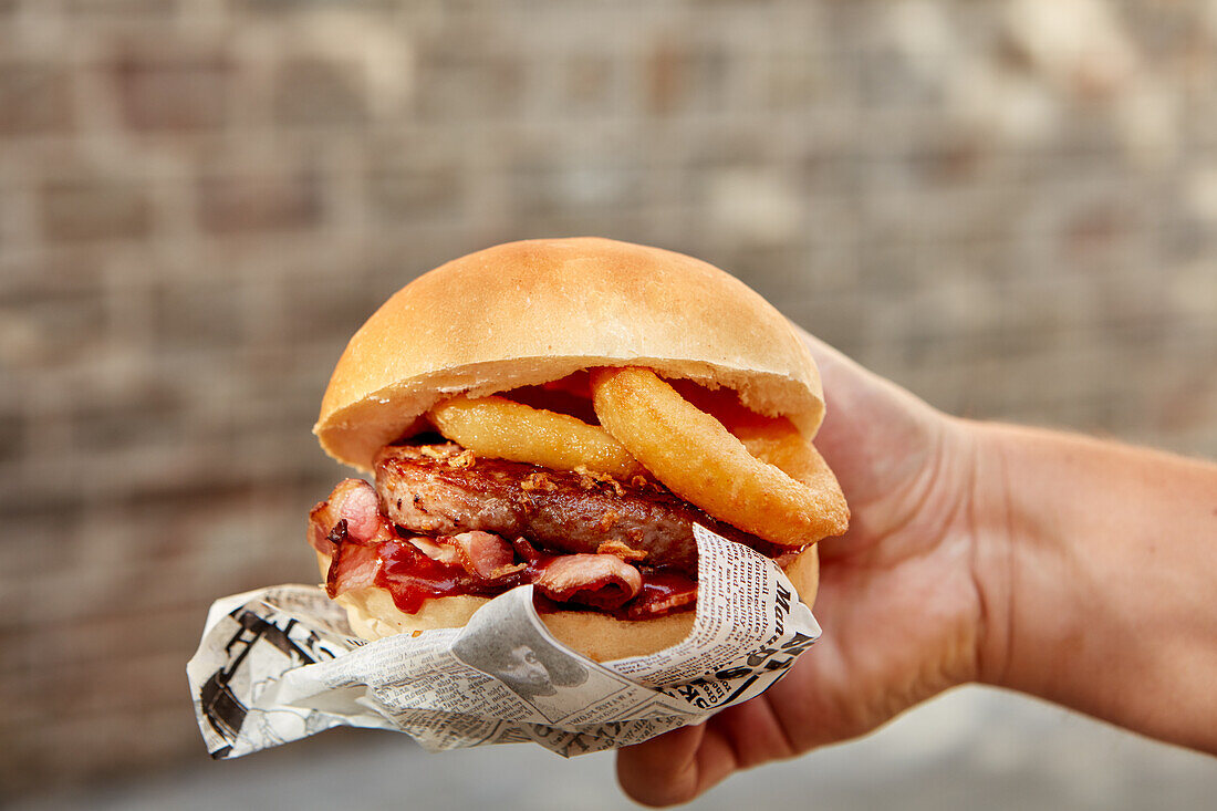 Hand holding a veal burger with breaded onion rings, bacon, and ketchup