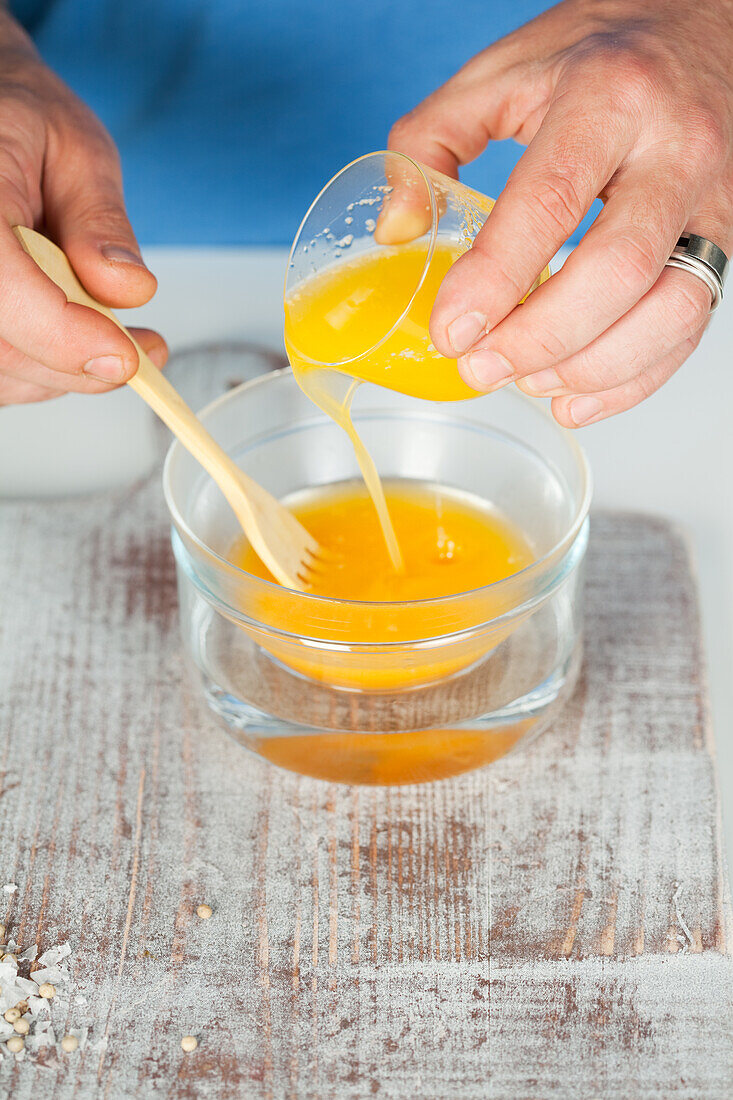 Zubereitung einer Sauce Hollandaise - geschmolzene Butter zum Eigelb rühren