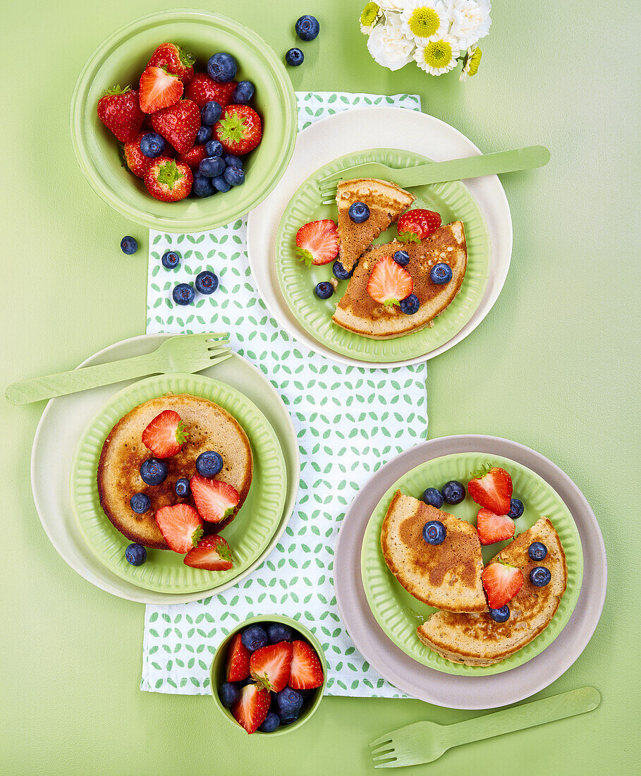 Pancakes mit Erdbeeren und Heidelbeeren auf grünem Untergrund