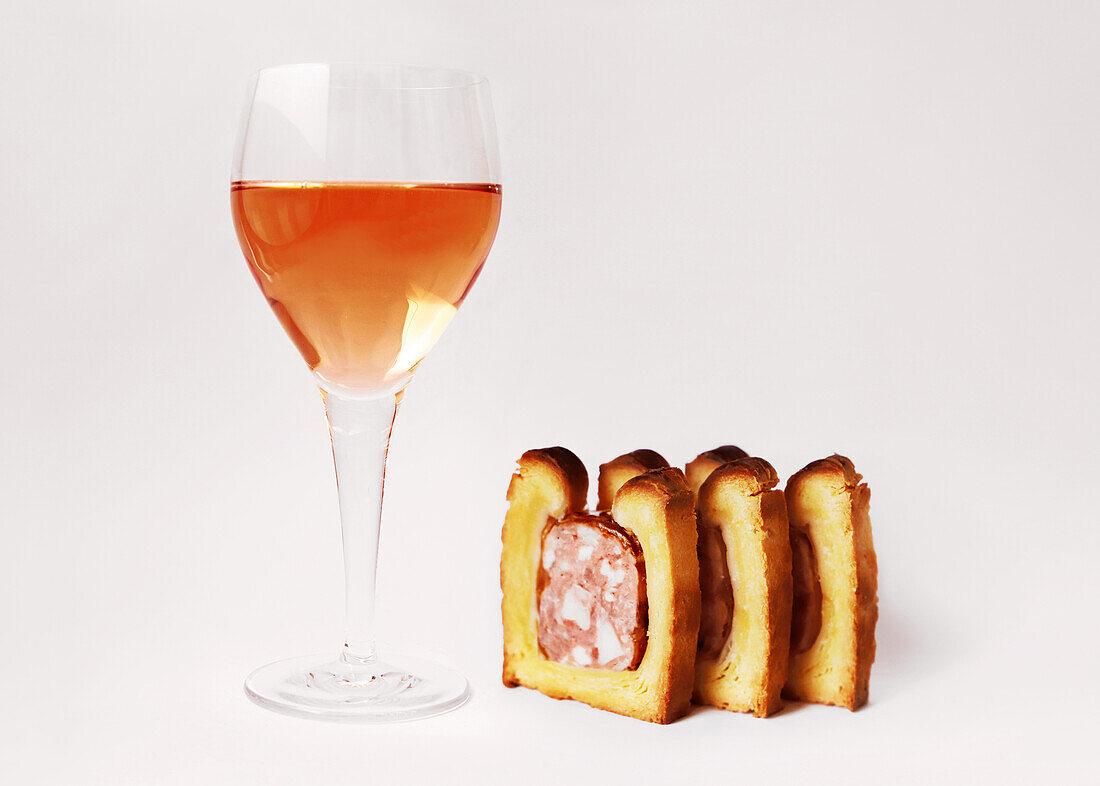 Drei Scheiben Fleisch-Pastete im Teigmantel daneben ein Glas Rosewein