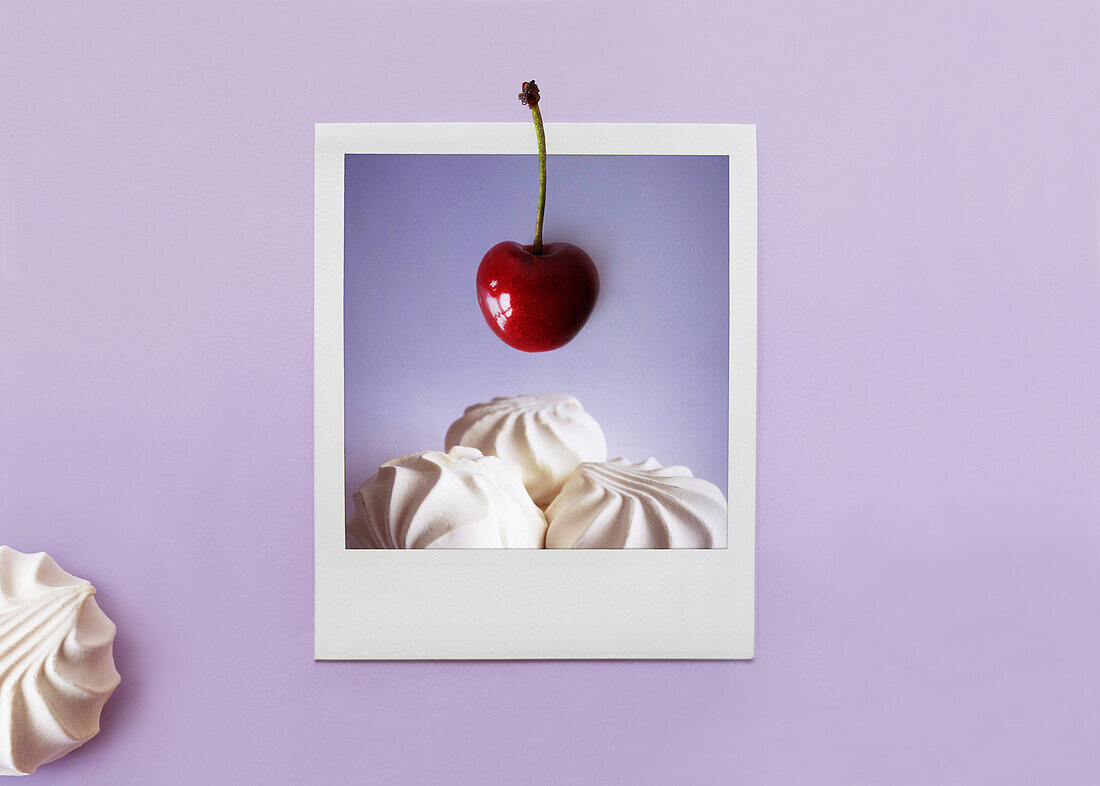 Polaroid photo of meringue with a cherry on top against a purple background
