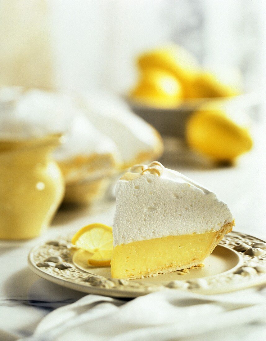Lemon Meringue PieSlice with Whole Pie and Bowl of Lemons