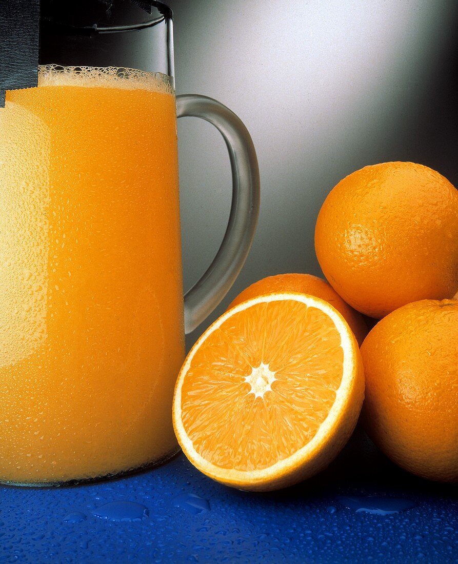 Ein Krug Orangensaft neben mehreren Valencia Orangen