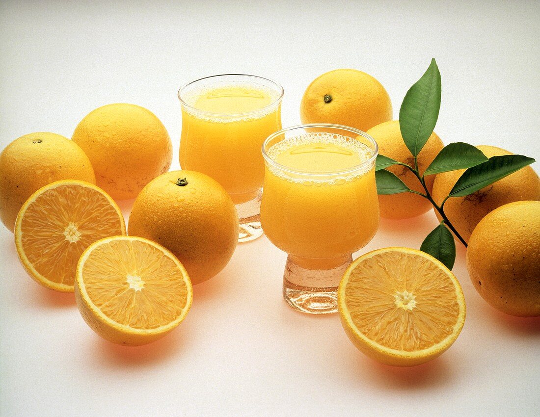 Zwei Gläser Orangensaft umgeben von mehreren Valencia Orangen