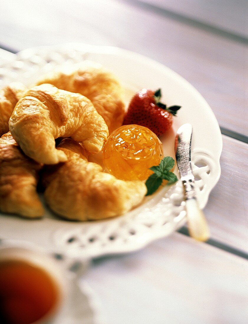 Croissants mit Orangenmarmelade, Erdbeere & Messer auf Teller