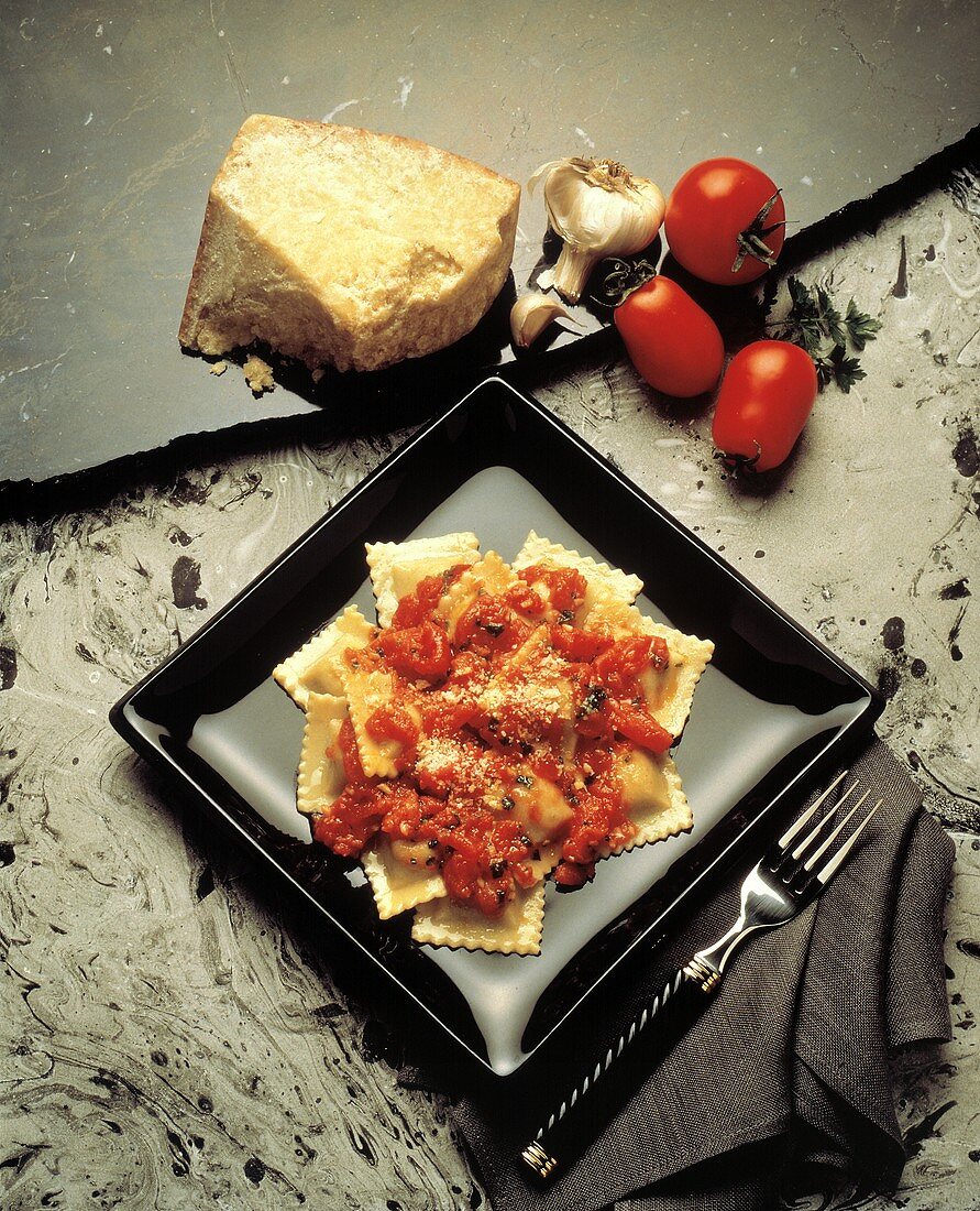 Ravioli mit Tomatensauce & Parmesan auf schwarzem Teller