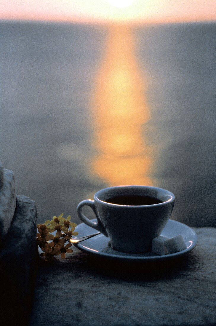 Eine Tasse Kaffee mit Zucker vor Sonnenuntergang am Meer