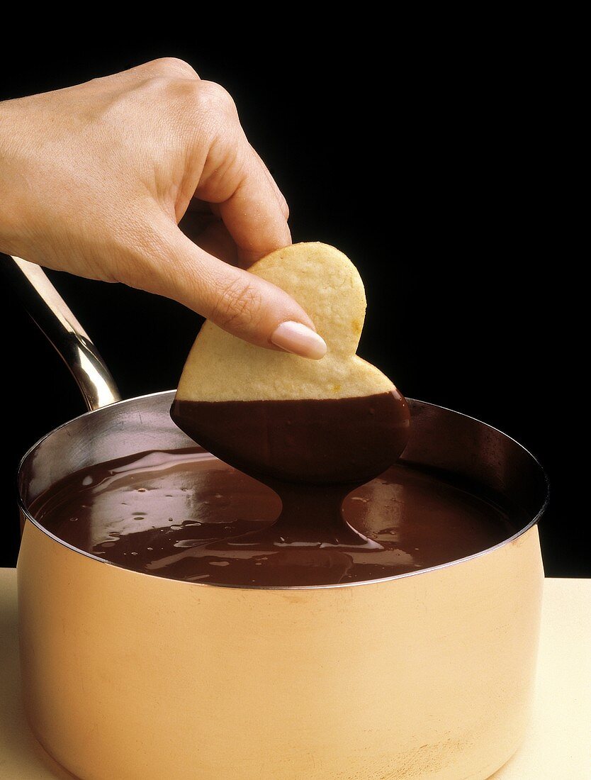 Herzförmiger Keks wird in flüssige Schokolade getaucht
