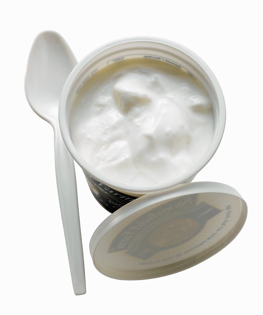 Joghurt in geöffnetem Joghurtbecher, daneben Plastiklöffel