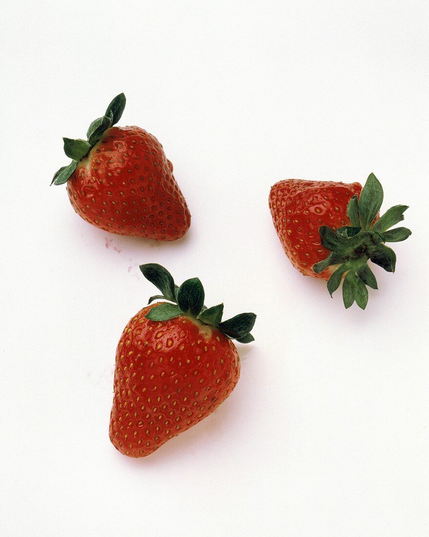 Drei ganze einzelne Erdbeeren auf weißem Untergrund