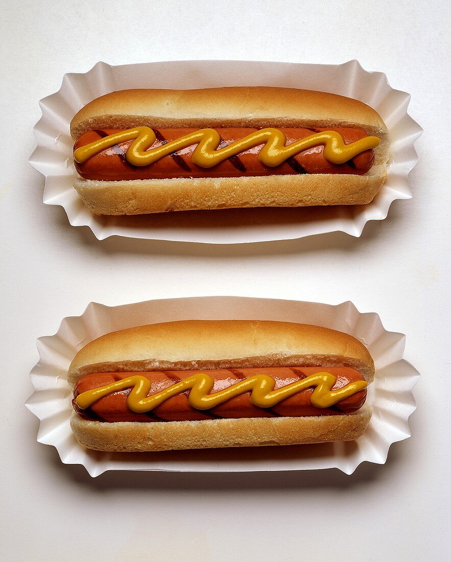 Zwei Hot Dogs mit Senf auf Papptellern