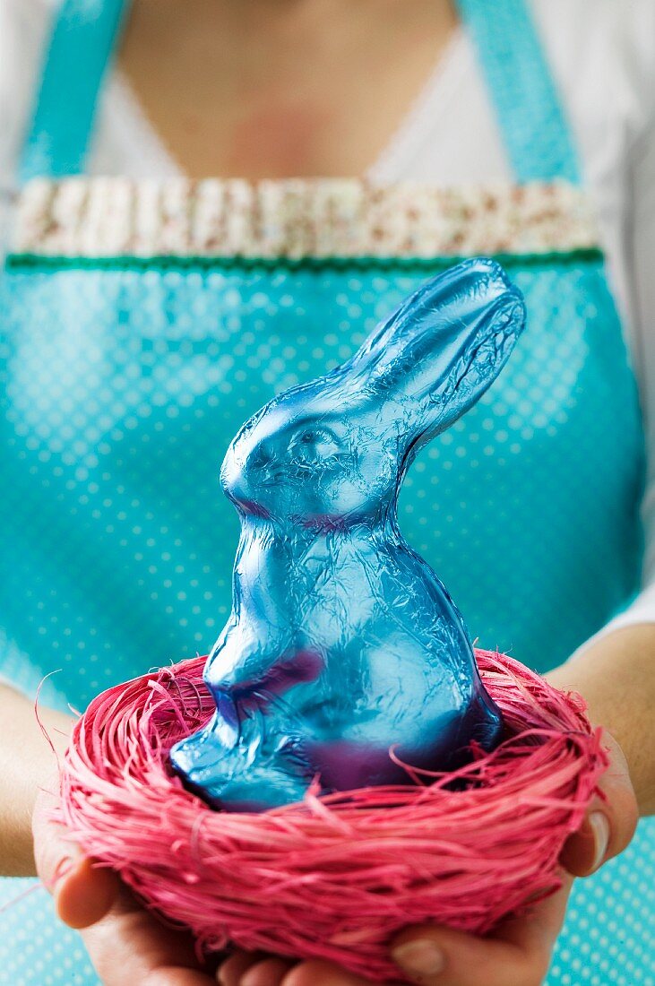 A woman holding an Easter nest with a blue chocolate bunny