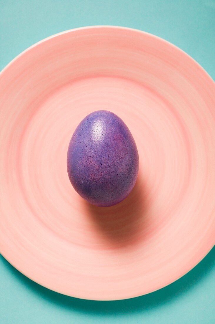 A purple Easter egg on a pink plate (seen from above)