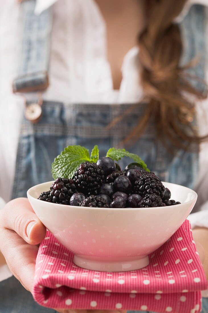 A woman holding a bowl of blackberries and blueberries