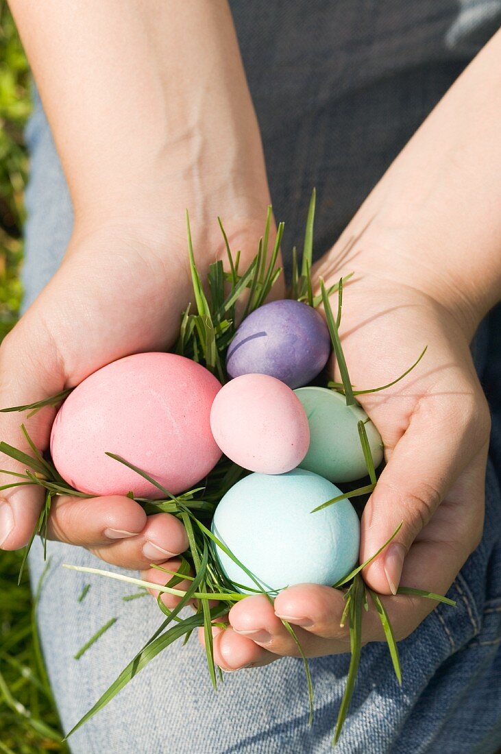 A woman holding coloured eggs on fresh grass
