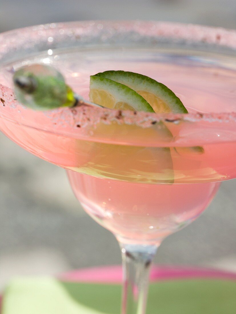 A pink drink with a slice of lime in a glass with a sugared edge