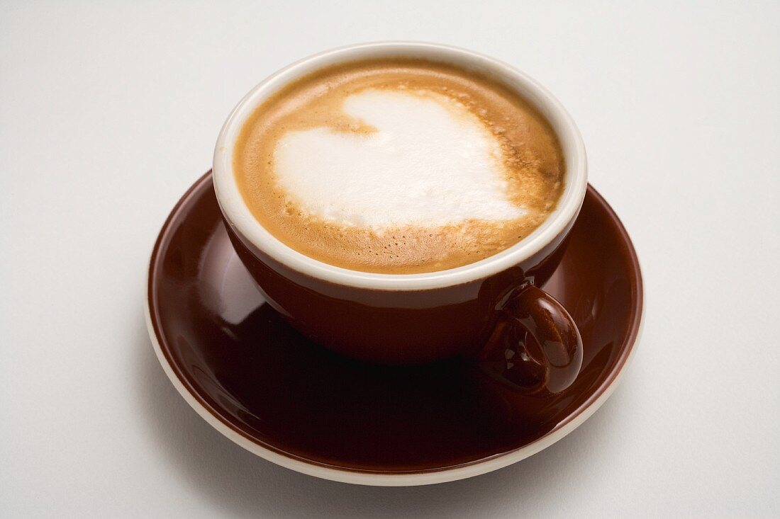 A cappuccino in a brown cup with a milk foam heart