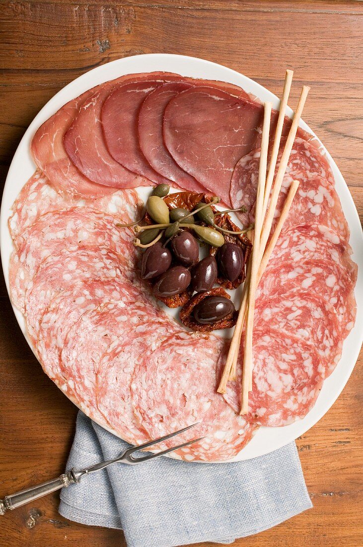 A meat platter with olives, capers and bread sticks (Italy)