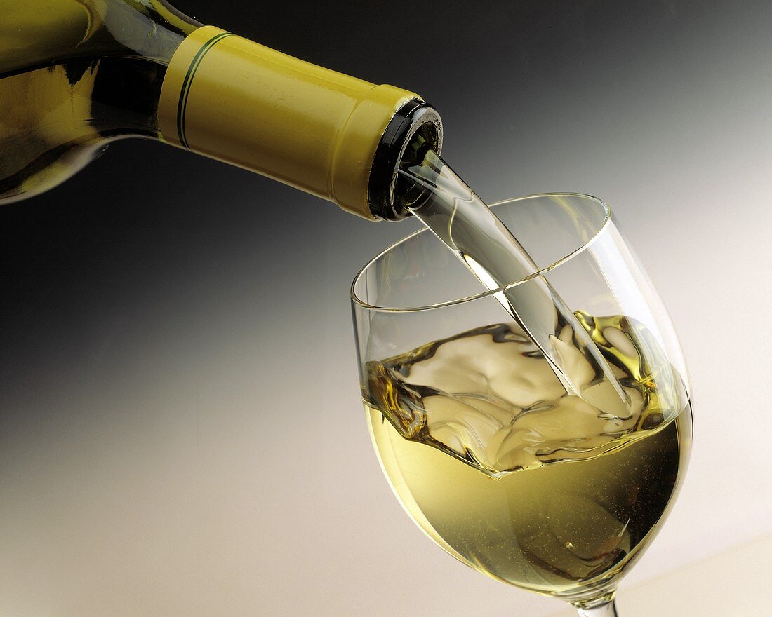 Weißwein aus Flasche in ein Glas einschenken
