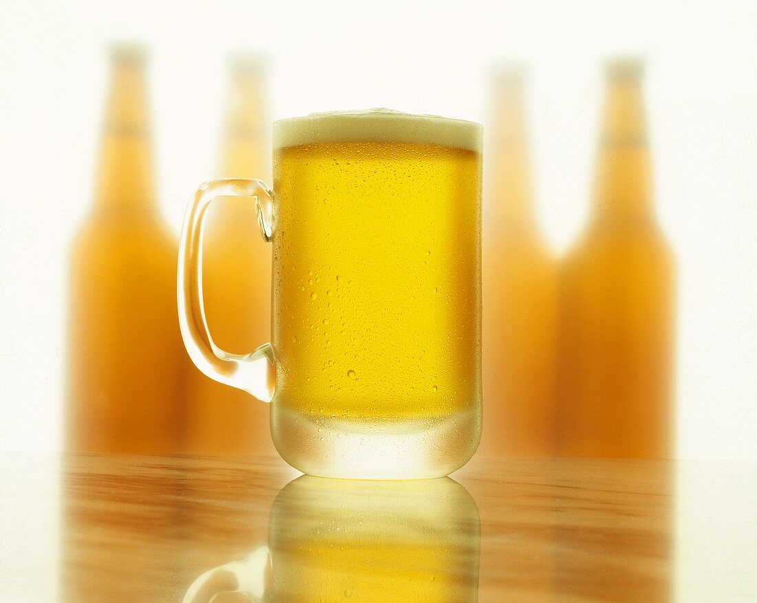 Kaltes Bier im Glaskrug; Flaschensilhouetten im Hintergrund