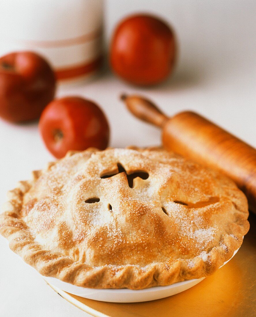 Frisch gebackene Applepie mit Zucker; rote Äpfel; Nudelholz