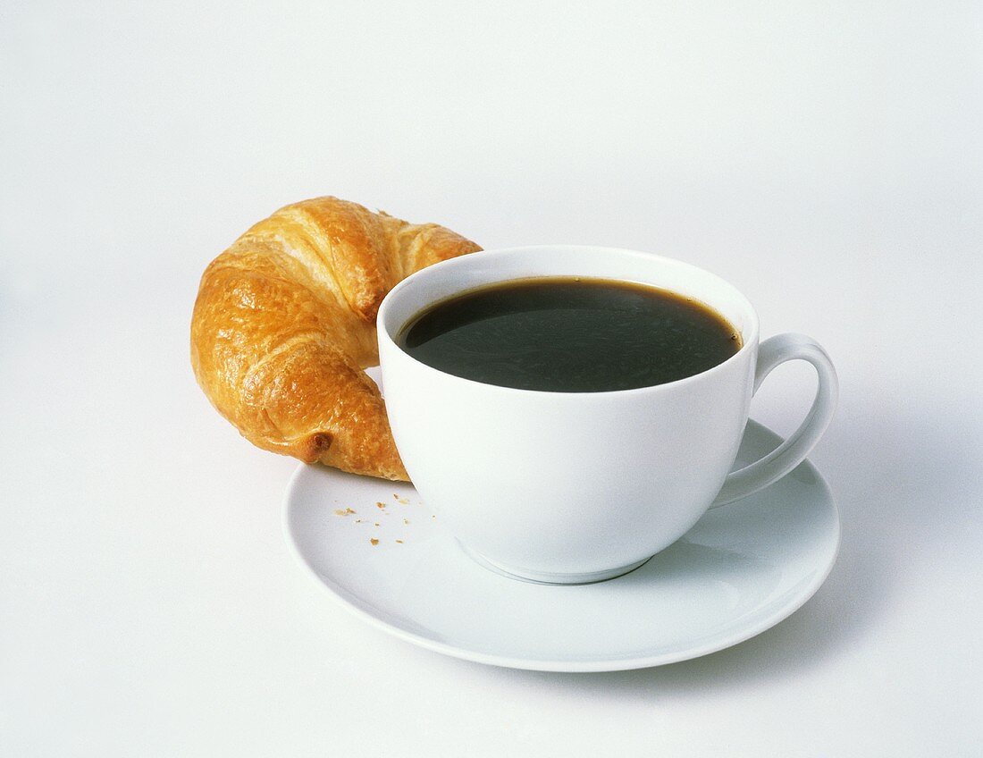 Tasse schwarzer Kaffe mit einem Croissant