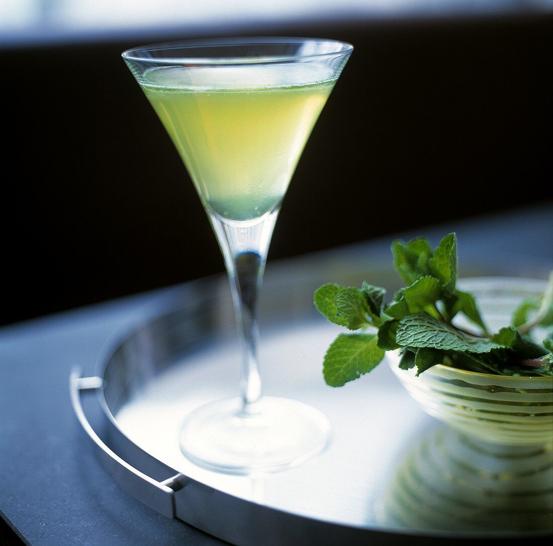 Ein Glas Mint-Cocktail, daneben Minzblätter