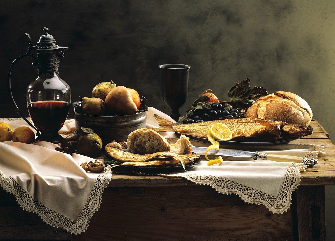 Gedeckter Tisch mit geräuchertem Fisch, Früchten, Wein & Brot