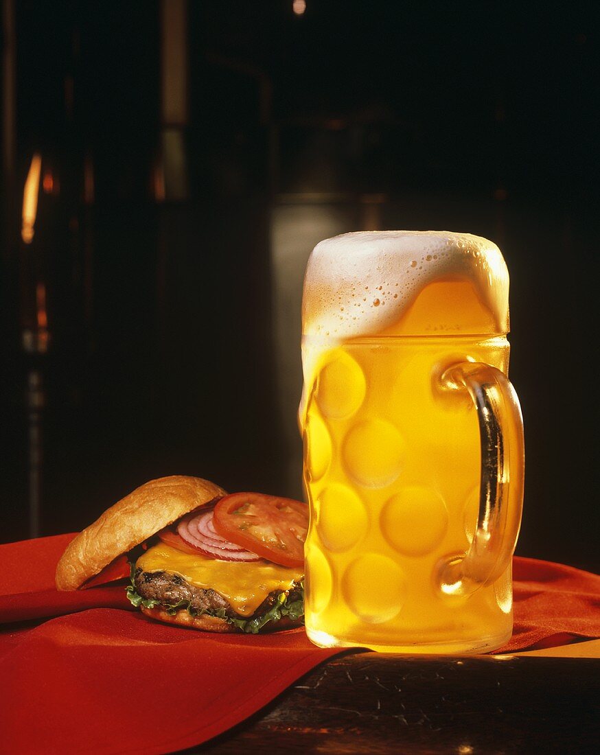 Überschäumendes Bier im Glaskrug neben Cheeseburger
